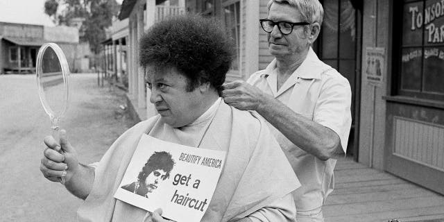 FILE - In this Aug. 15, 1968, file photo, comedian Marty Allen, fuzzy-haired member of the comedy team of Allen & Rossi, has his hair styled by barber Sol Goldstein in Hollywood, Calif. Allen's spokeswoman Candi Cazau says he died Monday, Feb. 12, 2018, of complications from pneumonia. His wife and performing partner Karon Kate Blackwell was by his side. He was 95. (AP Photo/Wally Fong, File)
