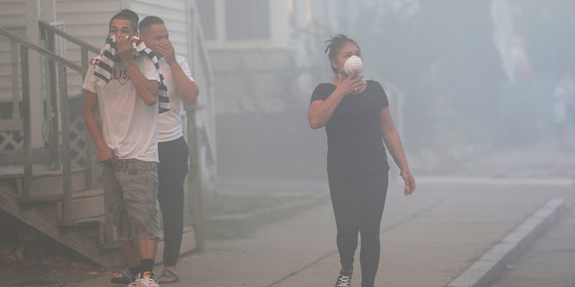 People cover their faces to protect themselves from heavy smoke from a fire on Bowdoin Street in Lawrence, Mass.