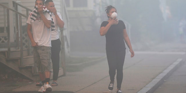 People cover their faces to protect themselves from heavy smoke from a fire on Bowdoin Street in Lawrence, Mass.