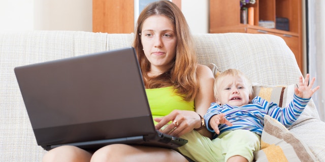 sorehead mother with crying toddler working online with laptop at home