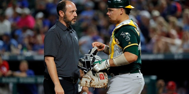 Oakland Athletics trainer Nick Paparesta, left, checks on catcher Bruce Maxwell after Maxwell was hit in the mask by a fouled ball off the bat of Texas Rangers' Ryan Rua in the fourth inning of a baseball game, Thursday, Sept. 28, 2017, in Arlington, Texas. (AP Photo/Tony Gutierrez)