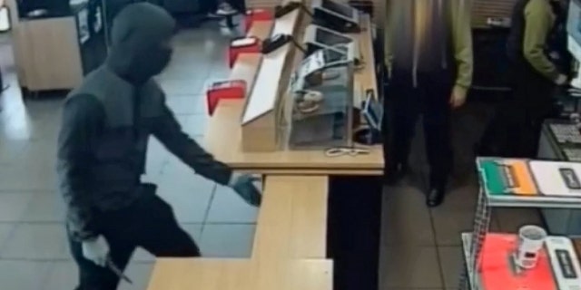 The suspect lifts up the barricade that separates the employees from the dining area, grabs the box, and threatens a worker with the weapon before fleeing the store.