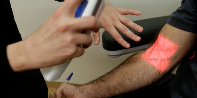 In this Jan. 10, 2017 photo, Adrian Aoun, founder and CEO of Forward, left, gives a demonstration of a vein illumination device that uses infrared light on an Associated Press reporter at a medical office in San Francisco. After a relative suffered a heart attack a few years ago, Silicon Valley entrepreneur Aoun got an up-close look at a health-care system that he diagnosed as an inefficient and outdated mess. Now, Aoun is ready to prescribe his remedy. It's called Forward, a health-management service that charges a $149 per month, roughly $1,800 a year, to tend to all of its patients' primary-care needs. (AP Photo/Jeff Chiu)