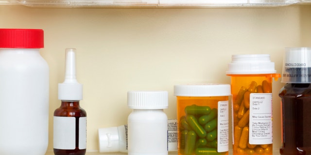 Several containers of over the counter and prescription medications on the shelves of a 1960's medicine cabinet.
