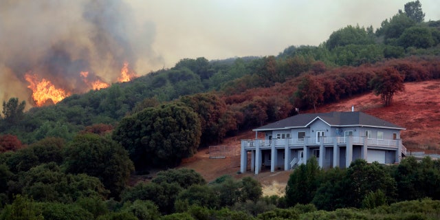 A wildfire crests over a ridge, threatening a home, bottom right, Monday, July 30, 2018, in Lakeport, Calif.