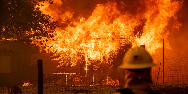 A firefighter monitors a burning outbuilding to ensure flames don't spread as the River Fire burns in Lakeport, Calif., on Monday, July 30, 2018.