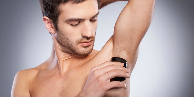 Staying fresh. Confident young shirtless man using dry deodorant while standing isolated on grey background