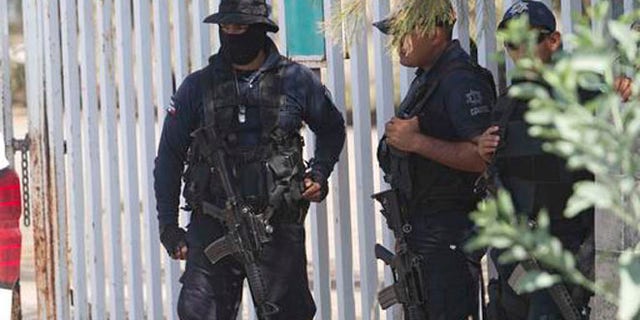 FILE - In this May 22, 2015, file photo, Mexican state police stand guard near the entrance of Rancho del Sol, where a shootout with the authorities and suspected criminals happened near Vista Hermosa, Mexico. Mexico's National Human Rights Commission said on Thursday, Aug. 18, 2016, that it has concluded that 22 people were arbitrarily executed by federal police during the event. Commission President Luis Raul Gonzalez Perez said their investigation revealed a range of human rights abuses on the part of government forces. (AP Photo/Refugio Ruiz, File)