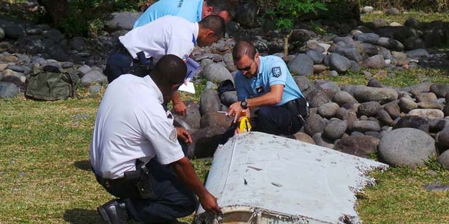 July 29: French gendarmes and police inspect a large piece of plane debris which was found on the beach in Saint-Andre, on the French Indian Ocean island of La Reunion.