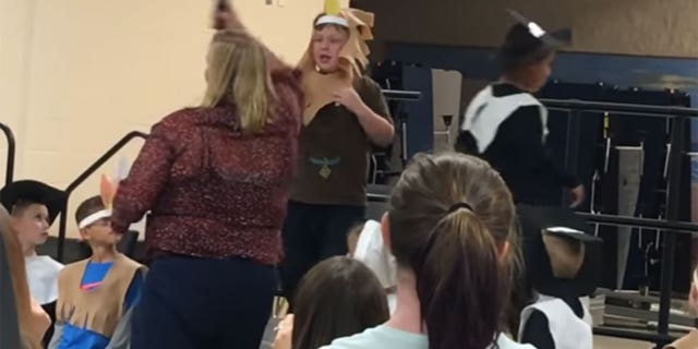 Caleb Riddle, 6, is shown on stage the moment a teacher tries to grab the microphone from its stand. The viral video of the incident has prompted backlash against the teacher.