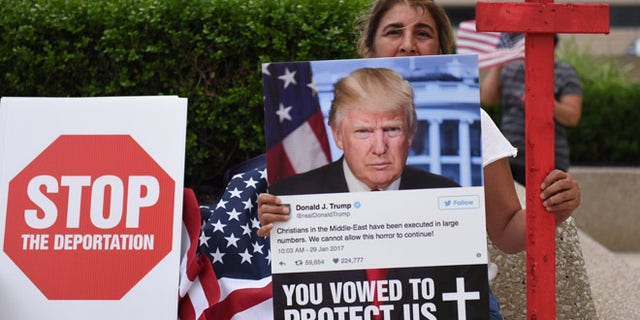 Amal Hana, of Warren, Mich., holds a photo of Donald Trump on Friday, June 16, 2017, outside the Patrick V. McNamara Federal Building during a protest in Detroit. Hana said a family member, whom she did not wish to name further, who has lived in the U.S. for 25 years was detained during the recent Immigration and Customs Enforcement raids of primarily Chaldean immigrants and is facing deportation. Hana joined hundreds others to protest the recent ICE raids in which more than 100 Iraqi nationals in Metro Detroit were detained. (Tanya Moutzalias/MLive.com via AP)