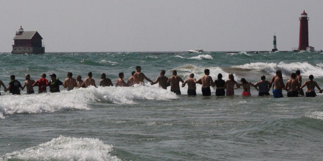 In this Aug. 5, 2018 photo, beachgoers help the Grand Haven Department of Public Safety officers form human chains to search for missing people in Lake Michigan at Grand Haven State Park in Grand Haven, Mich.