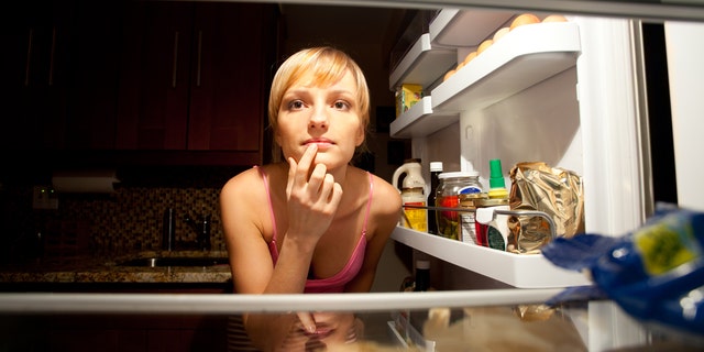Woman thinking about her food choice inside refregirator in kitchen at night