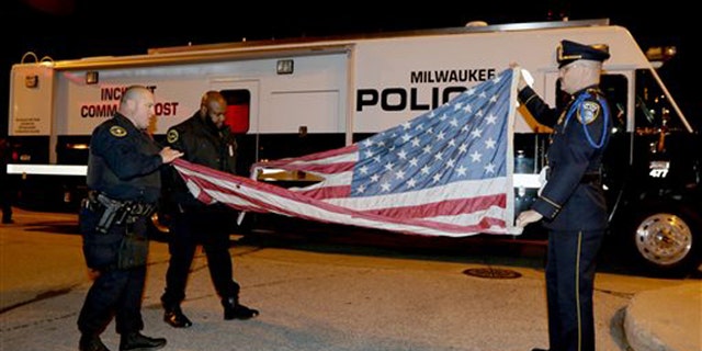 Nov. 10, 2015: In this provided by the Milwaukee Police Department, officers, from left, Jedidiah Thompson, Jutiki X and Joel Rossman fold a flag they recovered after it was set on fire by a protester outside the Republican presidential debate in Milwaukee.