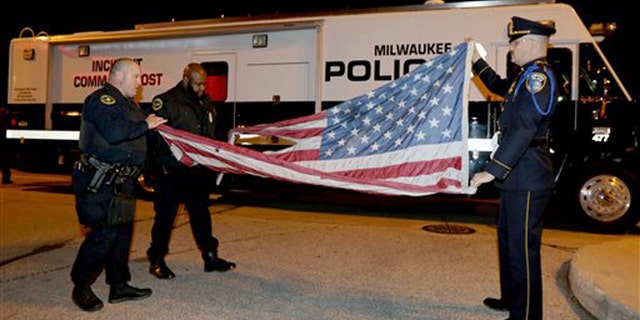 Nov. 10, 2015: In this provided by the Milwaukee Police Department, officers, from left, Jedidiah Thompson, Jutiki X and Joel Rossman fold a flag they recovered after it was set on fire by a protester outside the Republican presidential debate in Milwaukee.