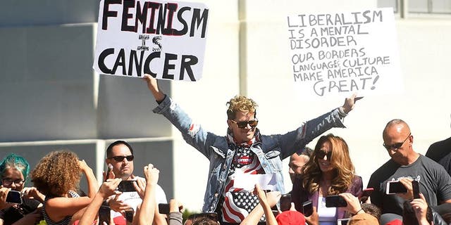 Milo Yiannopoulos holding protest signs while speaking at Berkeley last Sunday.