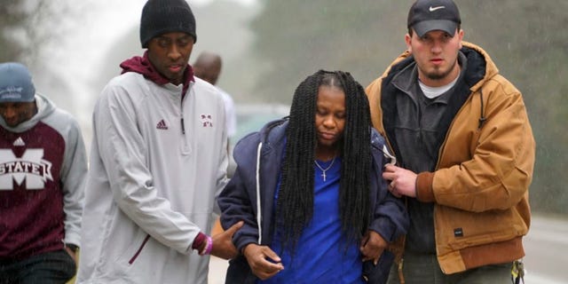 In this image taken Friday, Jan. 6, 2016, and released by Mississippi State Athletics, Mississippi State trainer Ryan Dotson, left, and an unidentified man aid a motorist who's car flipped over in front of the team bus in Mississippi, as they were heading to LSU for an NCAA college basketball game. (Drew Walker/Mississippi State Athletics via AP)