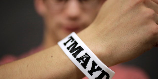 In this Monday, Feb. 1, 2016 photo, Massachusetts Institute of Technology student Andy Trattner, of Portland, Ore., displays a wrist band that features the acronym TMAYD for "Tell Me About Your Day," a campaign to encourage students to talk to one another in an effort to defuse to the stress of campus life before it leads to a crisis. There were several campus suicides last year. MIT officials recently set aside thousands of dollars for grants to help support campus projects dealing with mental health. (AP Photo/Steven Senne)