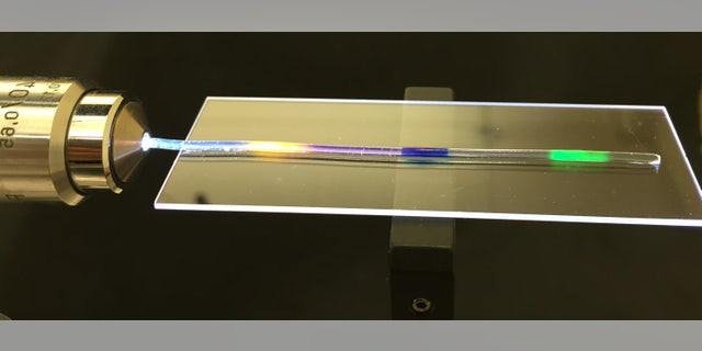 MIT researchers have developed a stretchy optical fiber in which they have injected multiple organic dyes (yellow, blue, and green regions). In addition to lighting up, the dyes act as a strain sensor, enabling researchers to quantify where and by how much a fiber has been stretched. (Courtesy of the researchers)