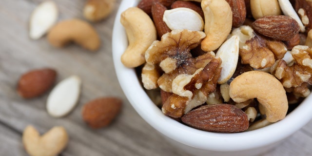 Bowl of mixed nuts on rustic wooden table in natural light.