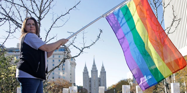 FILE - In this Nov. 14, 2015, file photo, Sandy Newcomb poses for a photograph with a rainbow flag as Mormons gather for a mass resignation from the Church of Jesus Christ of Latter-day Saints, in Salt Lake City. Mormon leaders are telling gay and lesbian church members that attraction to people of the same sex is not a sin or a measure of their faithfulness. But they are reminding those members that acting on those feelings by having sex violates fundamental doctrinal beliefs that won't change. The message is part of the Mormon church's "Mormon and Gay" website launched Tuesday, Oct. 25, 2016, with dozens of articles, teachings, videos and stories from Mormons who identify themselves as gay. (AP Photo/Rick Bowmer, File)
