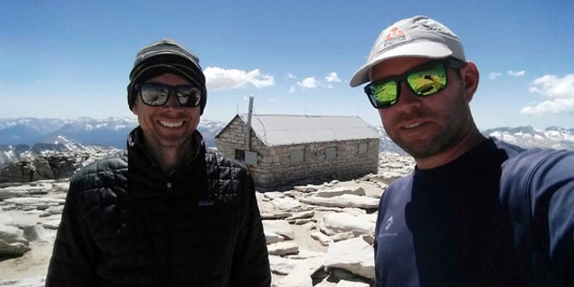 In this August 2017 photo provided by Brian McKinney, Sam Vonderheide, right, and McKinney, left, pose for a photo on the top of Mount Whitney, Calif. The two hikers walking a High Sierra trail videotaped a nerve-wracking stare-down with a wild mountain lion on July 23. The video shows the adult lion scurry down a winding trail out of sight; moments later the hikers round a turn to see the large cat peering down on them from a rocky perch feet away. (Brian McKinney via AP)