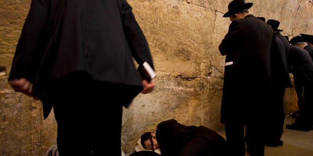 An Ultra-orthodox Jewish man sleeps as others pray during the mourning ritual of Tisha B'Av at the Western Wall, the holiest site where Jews can pray, in Jerusalem's Old City, Tuesday, Aug. 9, 2011. The Jewish holy day of Tisha B'Av, when Jews mourn the destruction of the biblical temples, is marked Tuesday. (AP Photo/Bernat Armangue)
