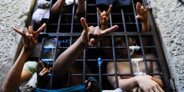 People arrested in El Salvador for being members of the MS-13 street gang flash their gang's hand signs from inside a jail cell.