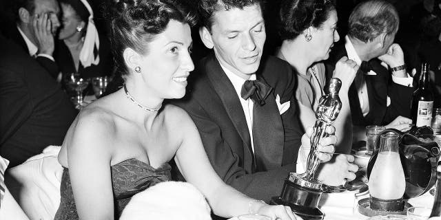 In this March 11, 1946 file photo, at a crowded table at Ciro's, Frank Sinatra steals a glance at his Oscar which he won for his performance in the film "The House I Live In," as his wife Nancy looks on at left.