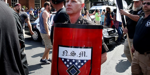 A white supremacist holds a shield with National Socialist Movement symbols on it as he arrives at a rally in Charlottesville, Va., Aug. 12, 2017.