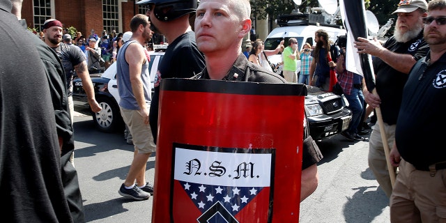 A white supremacist holds a shield with National Socialist Movement symbols on it as he arrives at a rally in Charlottesville, Va., Aug. 12, 2017.