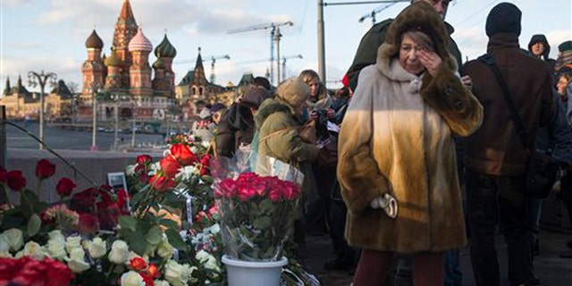 People lay flowers at the place where Russian opposition leader Boris Nemtsov was gunned down a year ago, marking the anniversary of his killing, in Moscow, with St. Basil Cathedral in the background, Russia, Saturday, Feb. 27, 2016. (AP Photo/Pavel Golovkin)