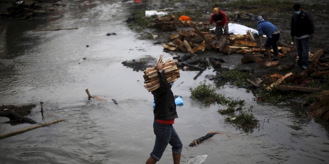 A man carries wood for pyre to burn the bodies of victims of Saturday's earthquake, during the cremation along a river in Kathmandu, Nepal April 28, 2015. REUTERS/Adnan Abidi - RTX1AOND
