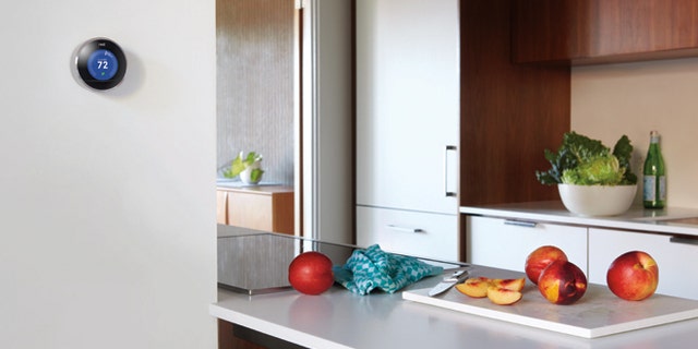 A Nest smart thermostat is seen on the wall of a kitchen.