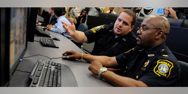 NEWARK, NJ - JULY 1: Communications clerk Angel Castro (L) demonstrates the movements of a remote surveillance camera to Lt. Darryl Martin in the newly-opened Surveillance Operations Center of the Newark, New Jersey Police Department before a press conference in Newark, July 1, 2008. (Photo by Jeff Zelevansky/Getty Images)