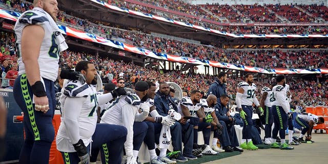 Seattle Seahawks players sit and kneel during the playing of the national anthem before a game against the San Francisco 49ers.