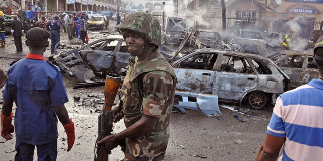 June, 25, 2014: In this file photo, a Nigerian soldier, center, walks, at the scene of an explosion in Abuja, Nigeria. A car bomb exploded in a market in Nigeria's northeastern city of Maiduguri on Tuesday morning, July 1, 2014  and dozens of people are feared dead, witnesses said.