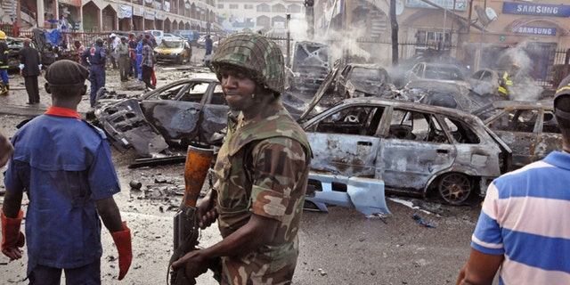 June, 25, 2014: In this file photo, a Nigerian soldier, center, walks, at the scene of an explosion in Abuja, Nigeria. A car bomb exploded in a market in Nigeria's northeastern city of Maiduguri on Tuesday morning, July 1, 2014 and dozens of people are feared dead, witnesses said.