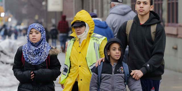 A crossing guard assists three Muslim school children at the end of a school day.