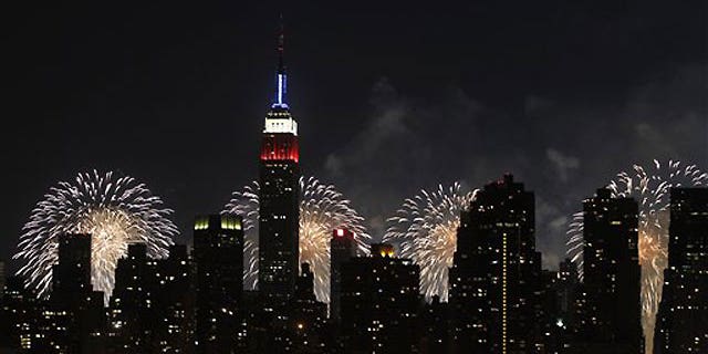 July 4: The Empire State Building, illuminated with red, white and blue lights, is seen from across the East River in the Queens borough of New York, and is backlit by fireworks exploding over the Hudson River during the Macy's Fourth of July fireworks show.