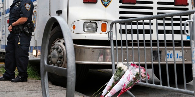 A police officer stands near the site where an officer was killed, and flowers have been left, in the Bronx section of New York, Thursday, July 6, 2017. Police officer Miosotis Familia was shot to death early Wednesday, ambushed inside her command post by an ex-convict, authorities said. He was later killed after pulling a gun on police. (AP Photo/Seth Wenig)