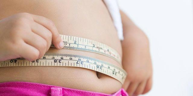 A person measures her waistline with measuring tape. 