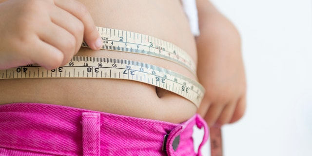 A person measures her waistline with measuring tape. 