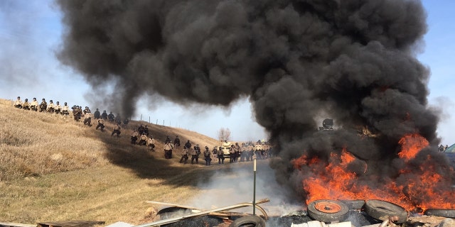 Tires burn as armed soldiers and law enforcement officers stand in formation on Thursday, Oct. 27, 2016, to force Dakota Access pipeline protesters off private land where they had camped to block construction. The pipeline is to carry oil from western North Dakota through South Dakota and Iowa to an existing pipeline in Patoka, Ill. (Mike McCleary/The Bismarck Tribune via AP)