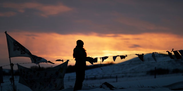 A woman watches the sunset at the Oceti Sakowin camp where people have gathered to protest the Dakota Access oil pipeline in Cannon Ball, N.D., Friday, Dec. 2, 2016.