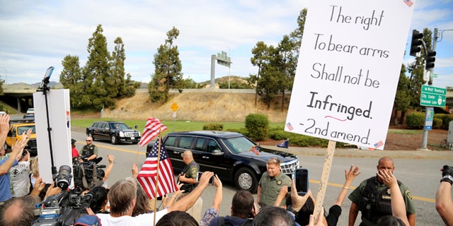 In this Oct. 9, 2015, photo, demonstrators wave flags and signs as President Obama's motorcade drives by in Roseburg, Ore.