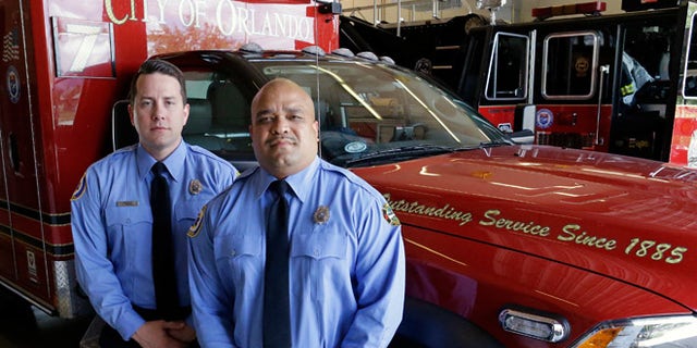 In this Thursday, June 30, 2016 photo, Josh Granada, left, and Carlos Tavarez the first paramedic-firefighters to respond to the Pulse nightclub shooting stand by their emergency vehicle at their fire station in Orlando, Fla. They made five trips with 13 victims to a hospital emergency room just a few blocks away the evening of the shooting.(AP Photo/John Raoux)