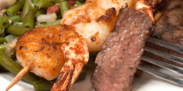 Closeup of sirloin steak on fork with shrimp on skewer and green beans.