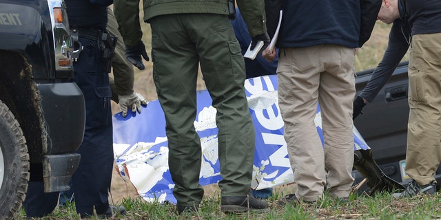 National Transportation Safety Board investigators examine a piece of debris from the plane that made an emergency landing Tuesday after a fatal engine mishap in Penn Township, Berks County, Pa.