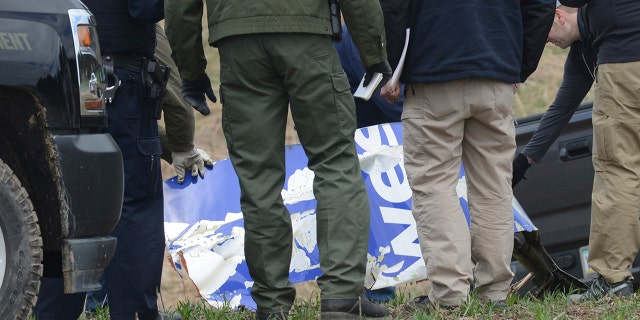 National Transportation Safety Board investigators examine a piece of debris from the plane that made an emergency landing Tuesday after a fatal engine mishap in Penn Township, Berks County, Pa.